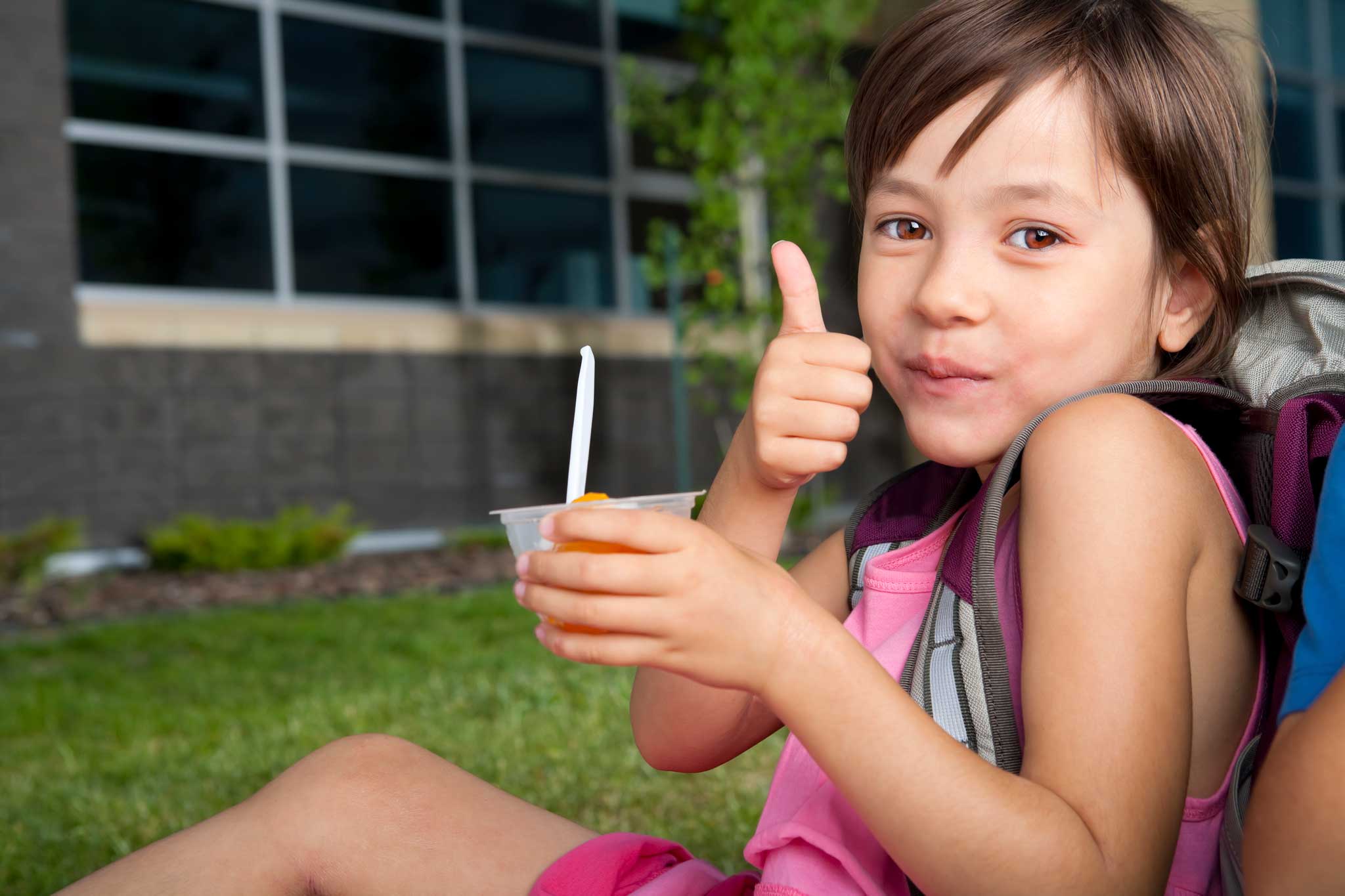 A young child eating peaches gives a thumbs up to the camera.