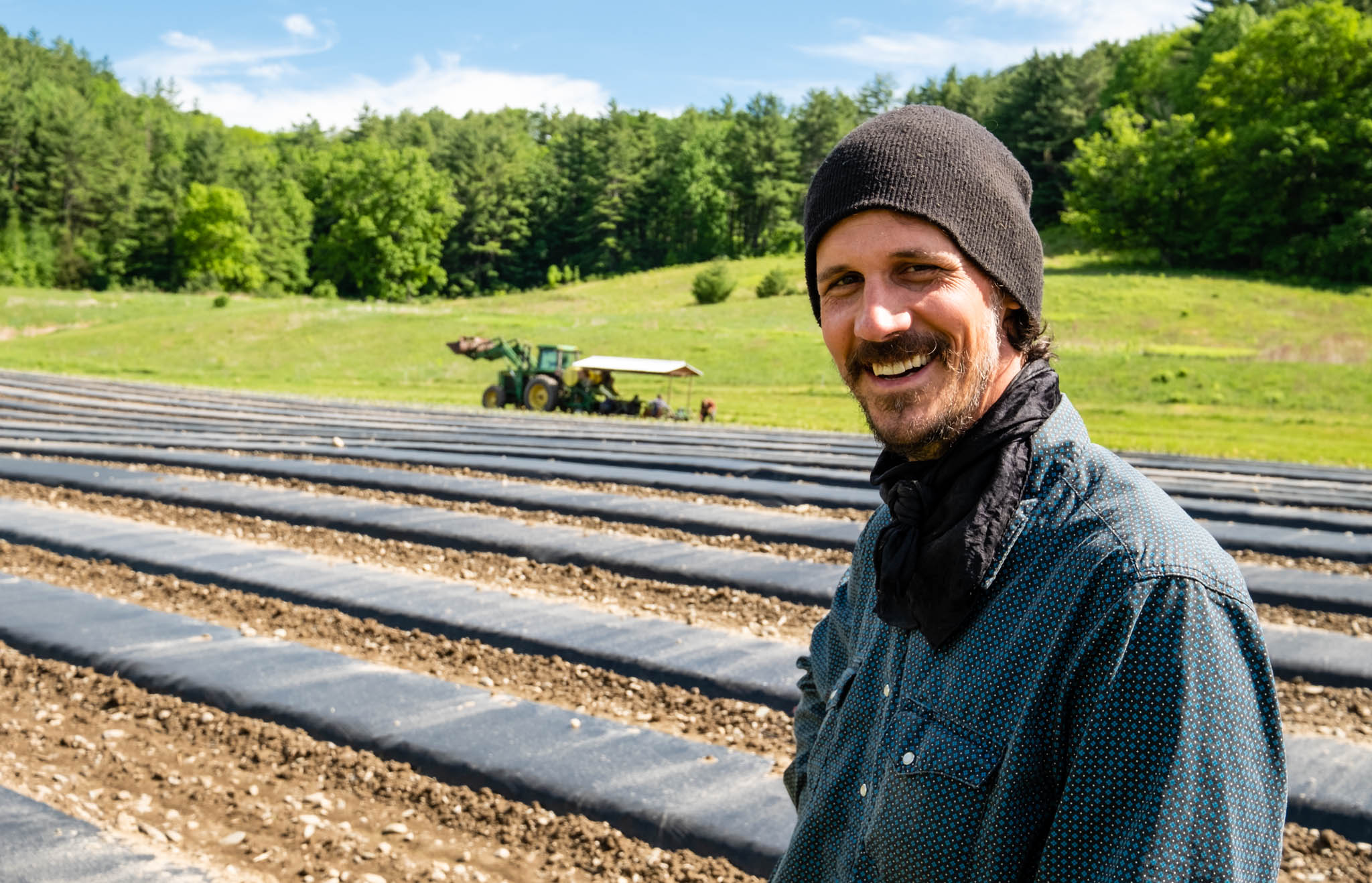 Photo of a farmer in a field with a tractor in the background. Vermont Foodbank works with farms throughout the state to negotiate produce purchases for the Vermonters Feeding Vermonters program.
