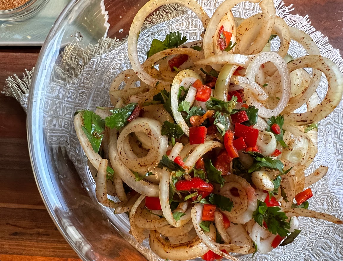 Sliced onions mixed with peppers, herbs and seasoning in a bowl