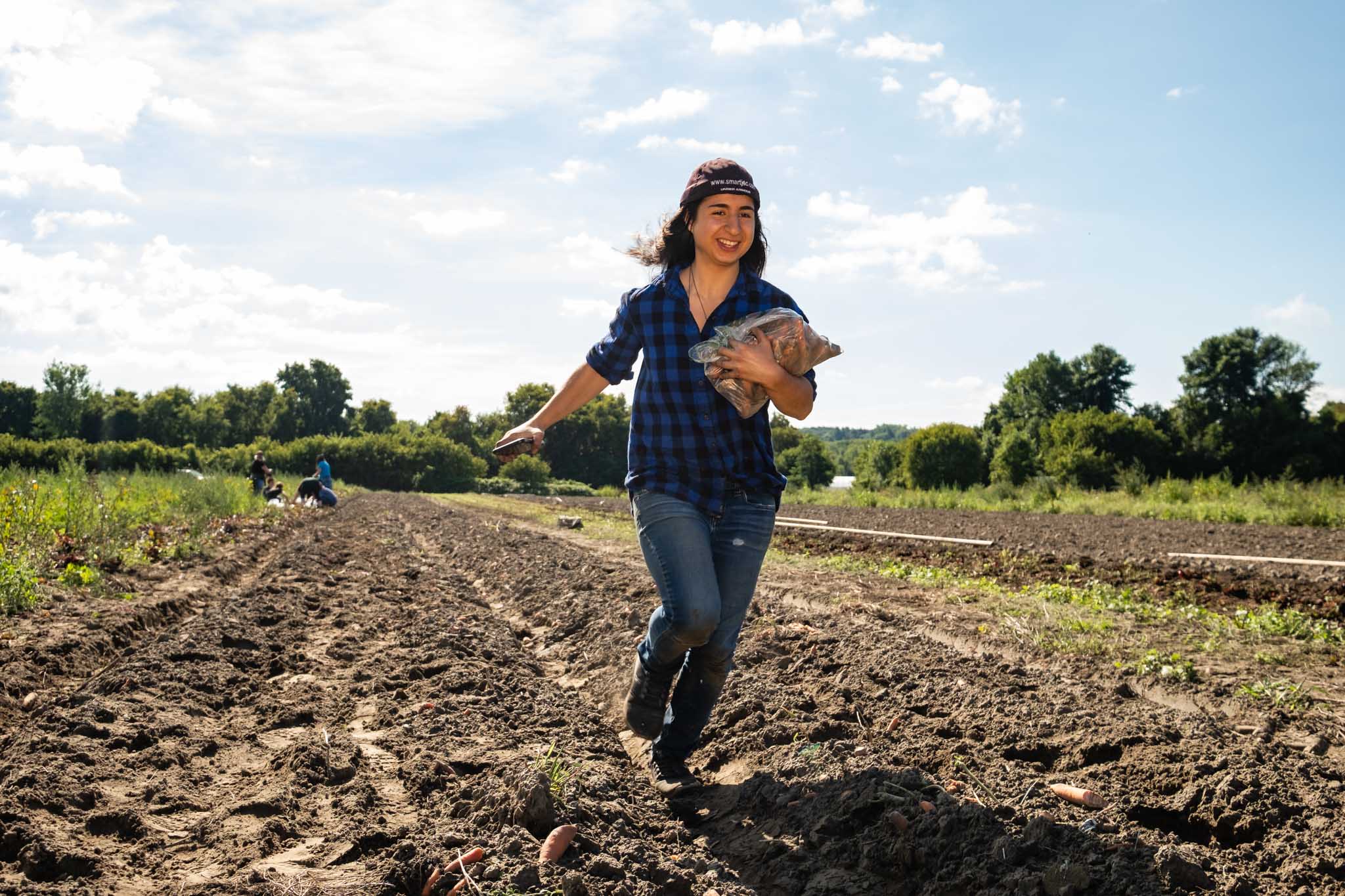 Photo of a woman running through a field with a bag of beets.