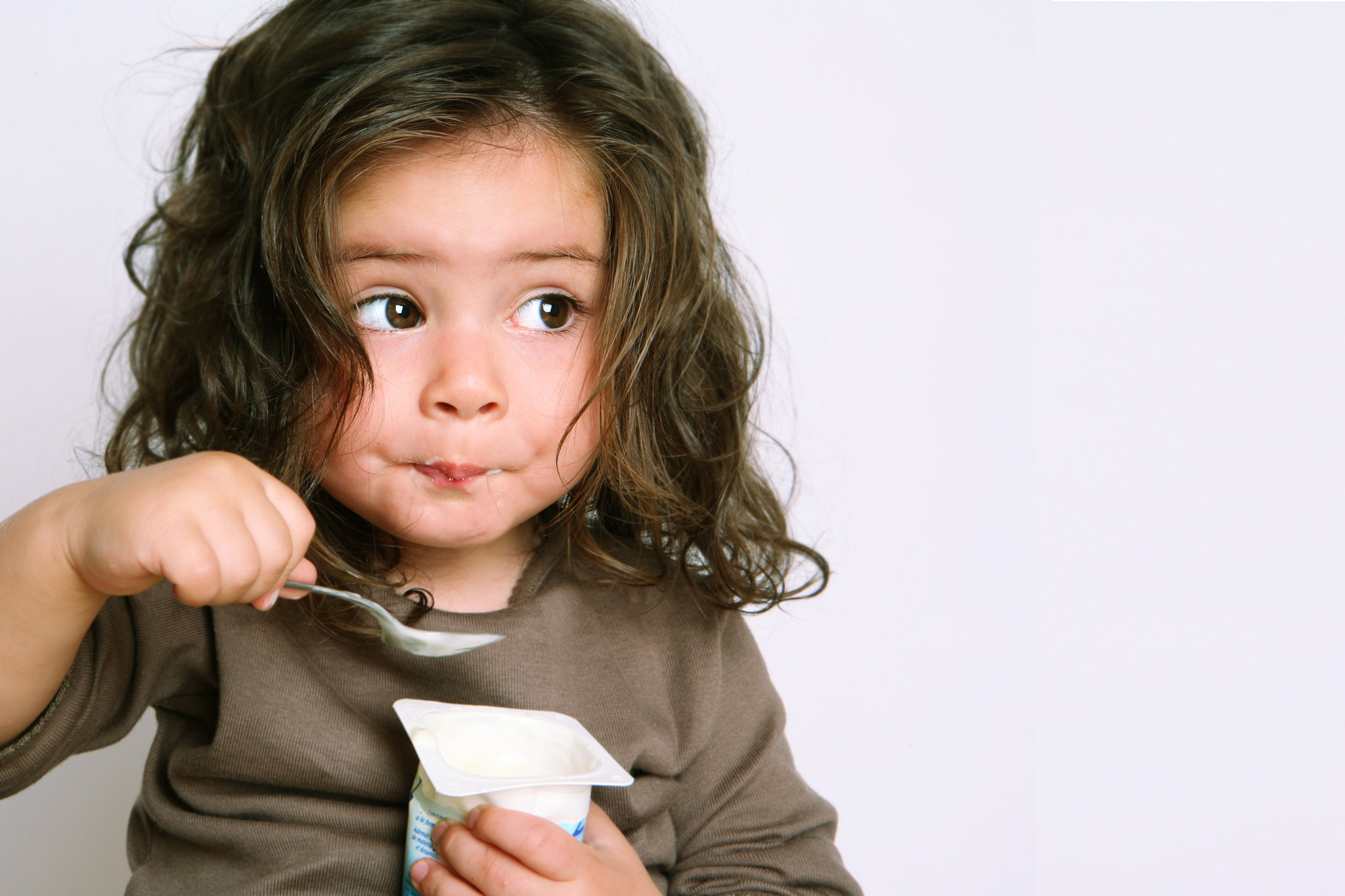 Young girl eating yogurt with a funny look on her face.