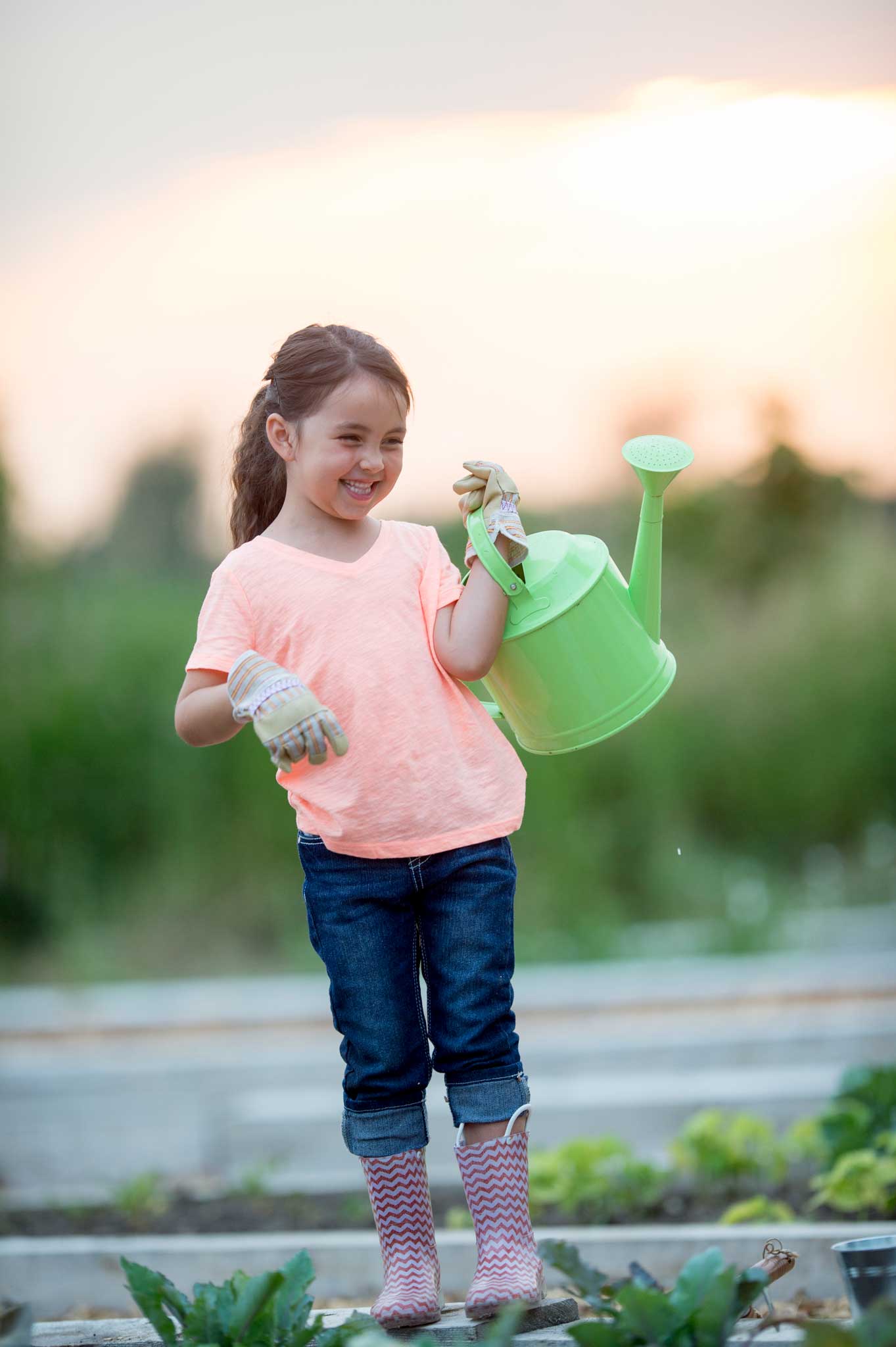 Photo of a young girl holding a watering can in a farm field.