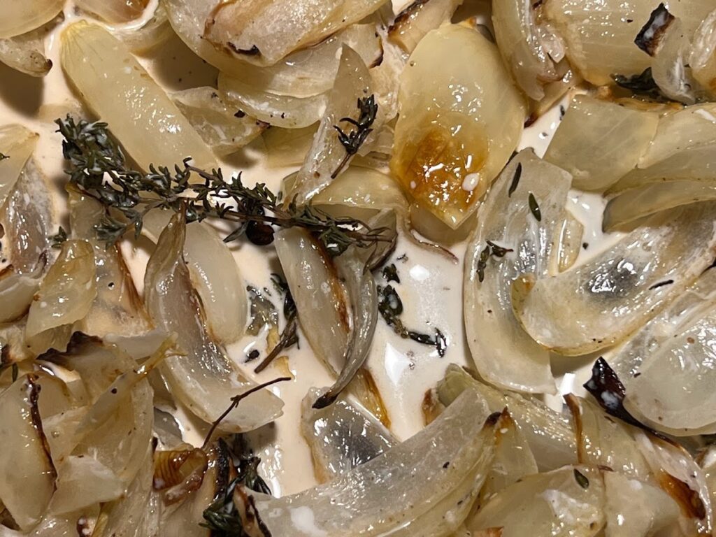 Photo of roasted onions and fresh thyme with cream added on baking sheet