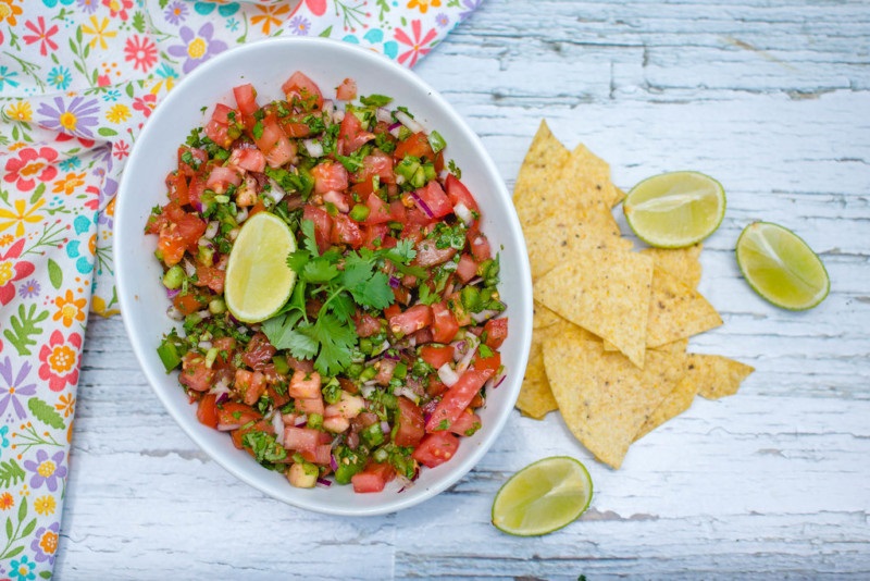 fresh salsa in a bowl with chips and limes on the side