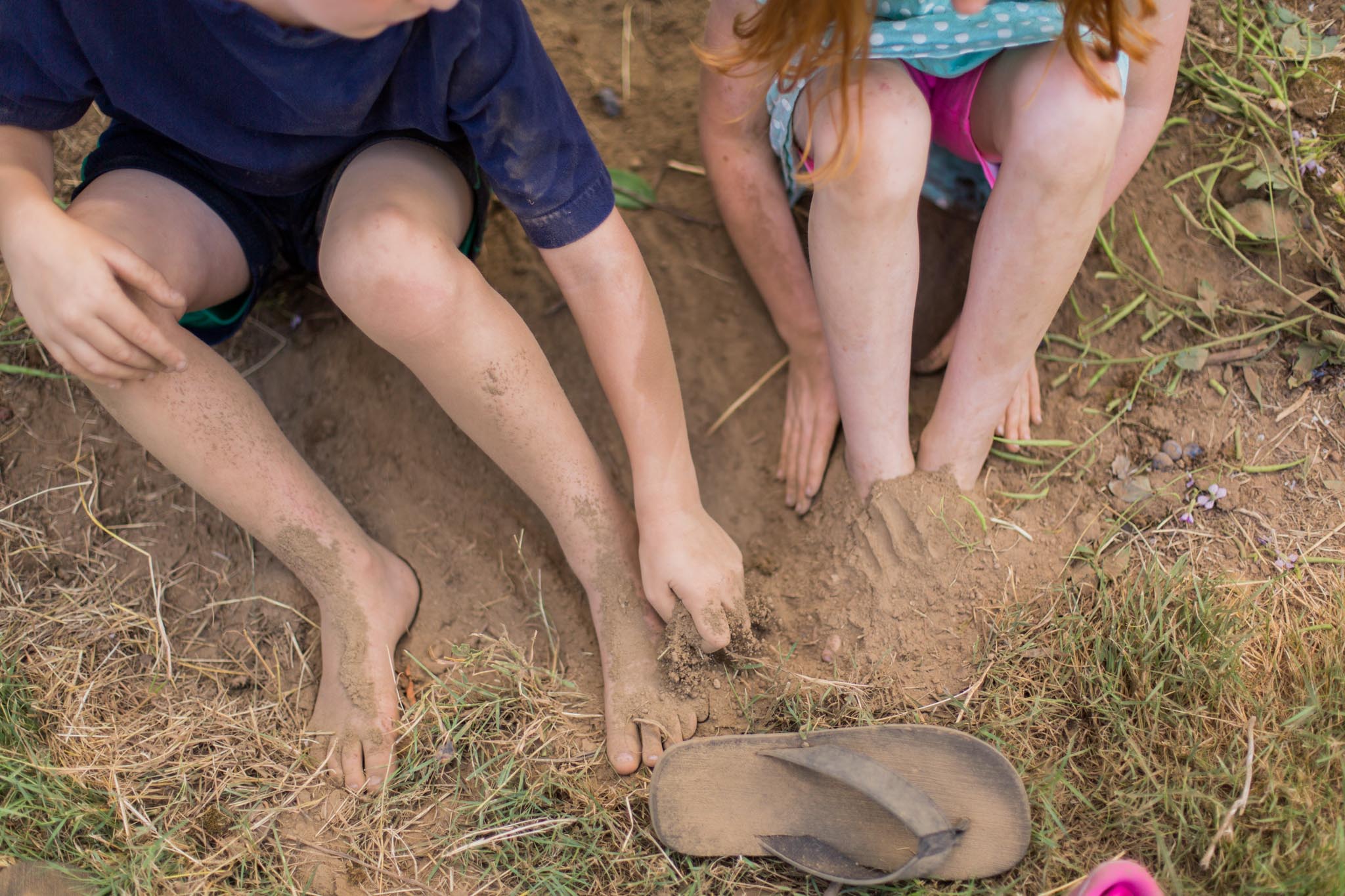 Photo of two kids playing in the dirt; only their legs and feet are visible.