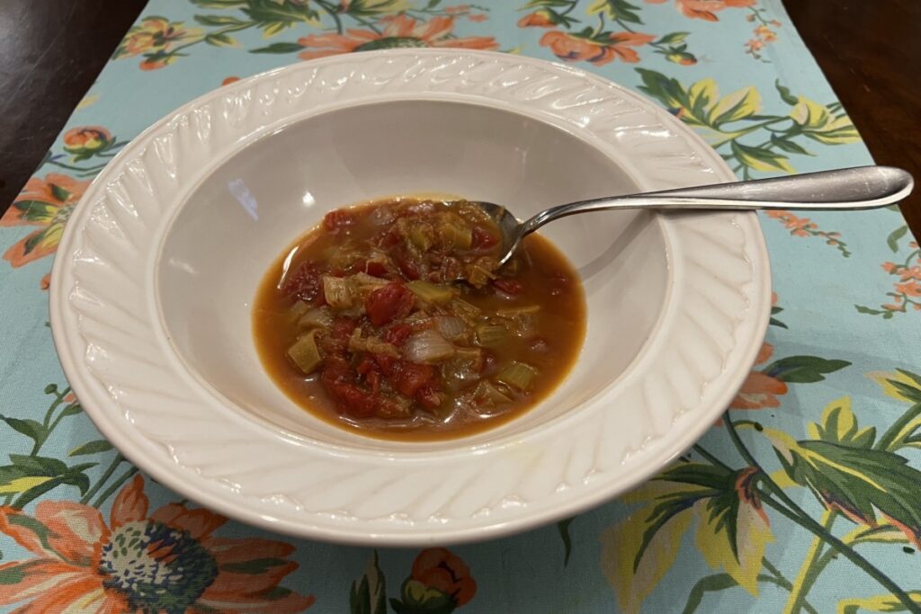 Photo of Rhubarb and Tomato Stew in white bowl with serving spoon on floral runner